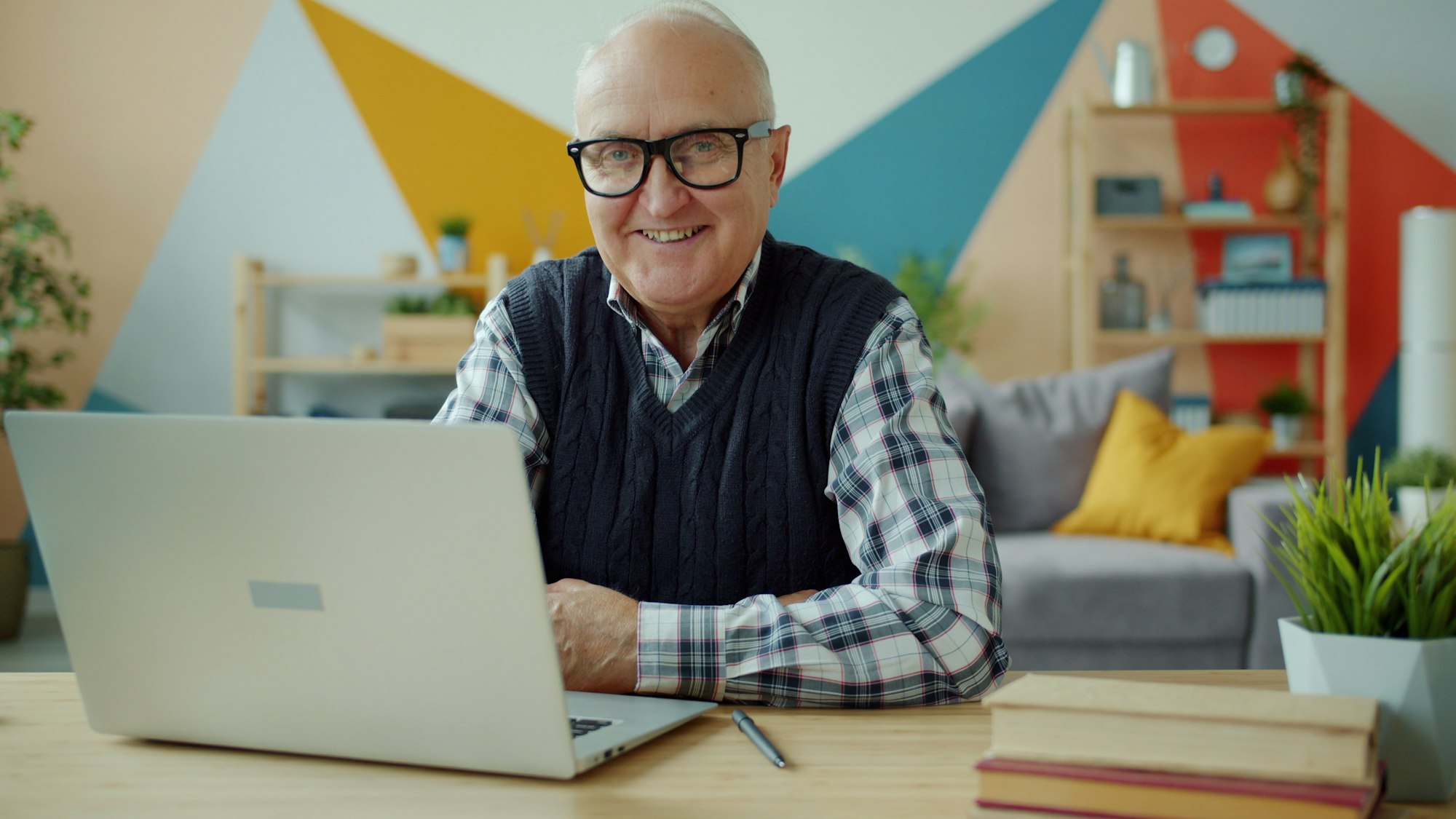A man at a desk with a laptop, smiling at the camera
